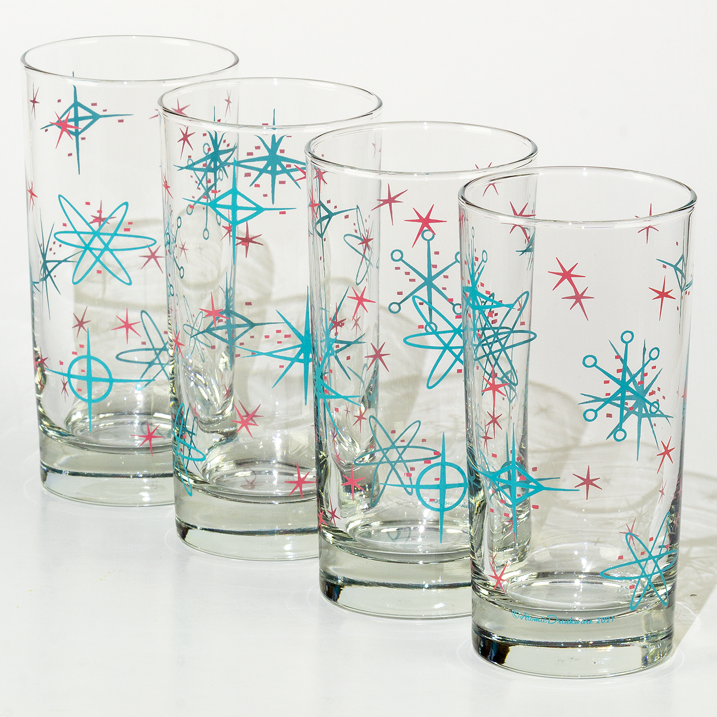 Four mid century modern glasses with blue and red atomic retro starburst patterns on a white background