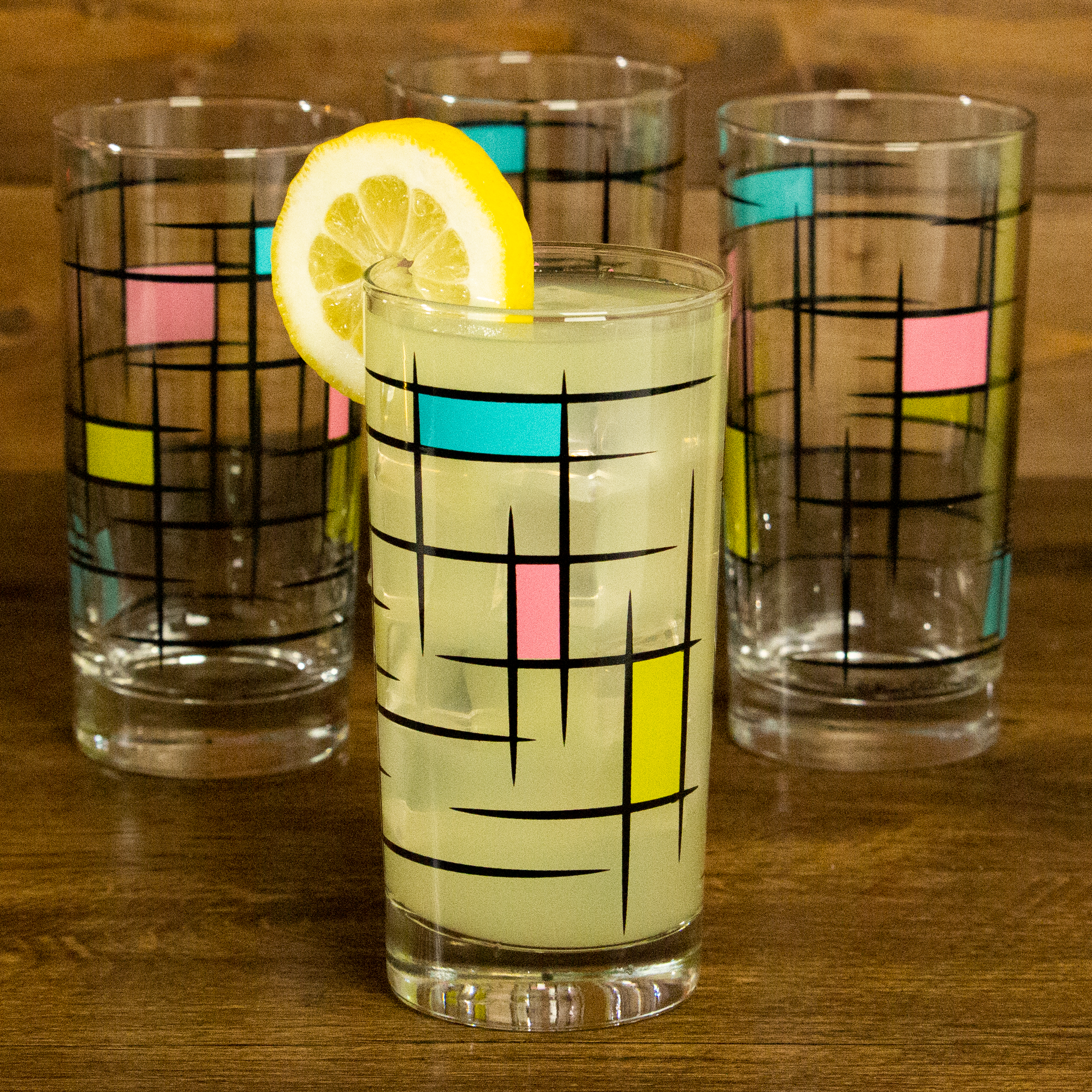 Set of four brutalist mid century modern collins glasses on a wooden surface with a lemon wedge.