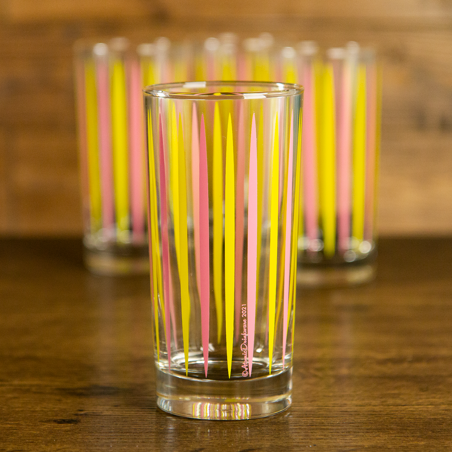 Mid-century modern cocktail glassware with retro pink and yellow striped cosmic rays on a wooden surface