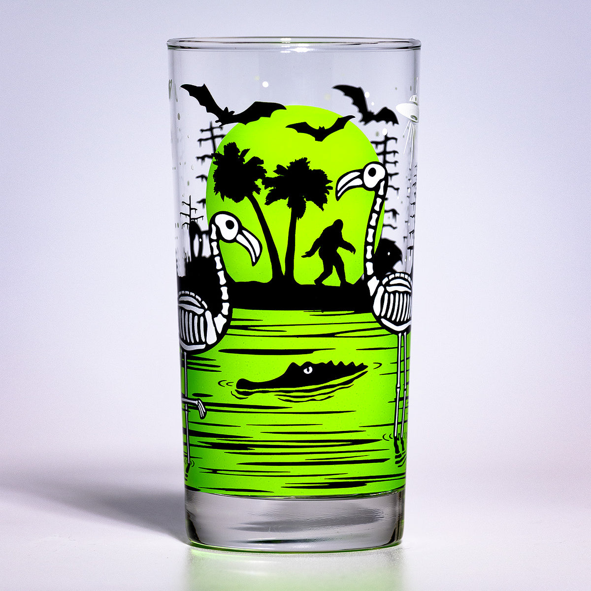 UV Fluorescent Chartreuse green Eerie Everglades Collins single glass with black spooky swamp silhouettes and glow-in-the-dark skeleton flamingos, skelemingos, on a white background.