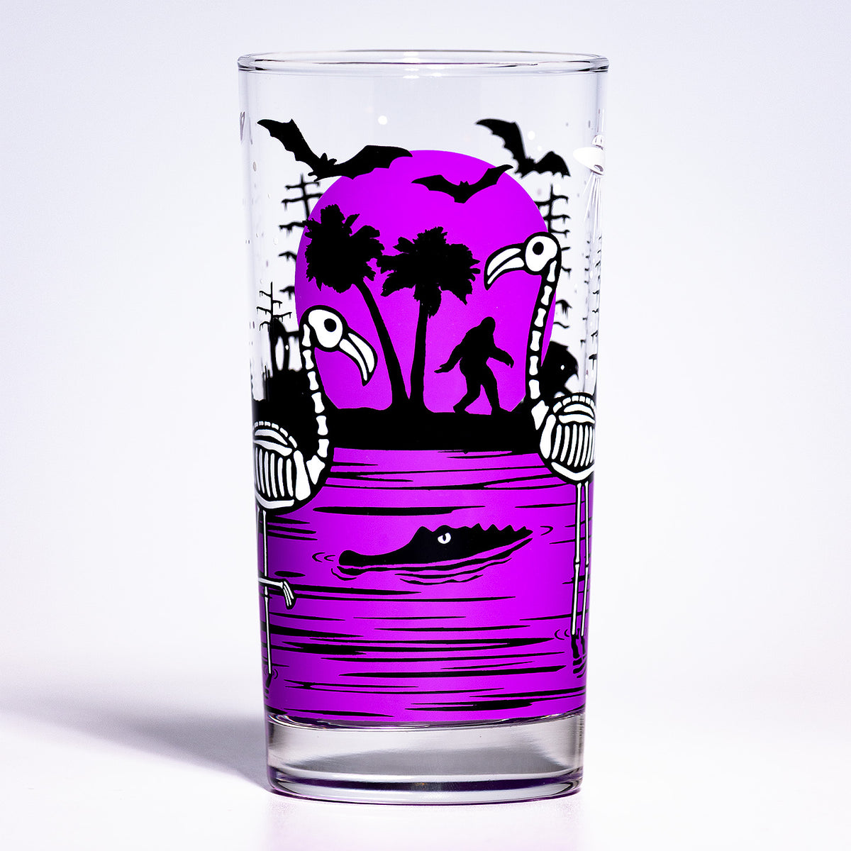 UV Fluorescent Purple Eerie Everglades Collins single glass with black spooky swamp silhouettes and glow-in-the-dark skeleton flamingos, skelemingos, on a white background.