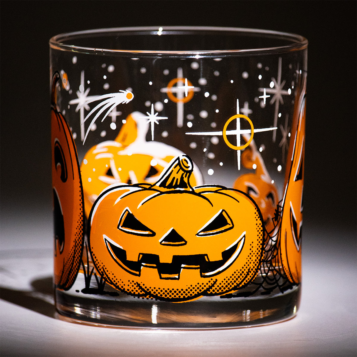 Five Little Pumpkins Rocks glass with retro style hand illustrated jack-o-lantern with shooting stars on a dark background.  Squat devilish looking Halloween pumpkin