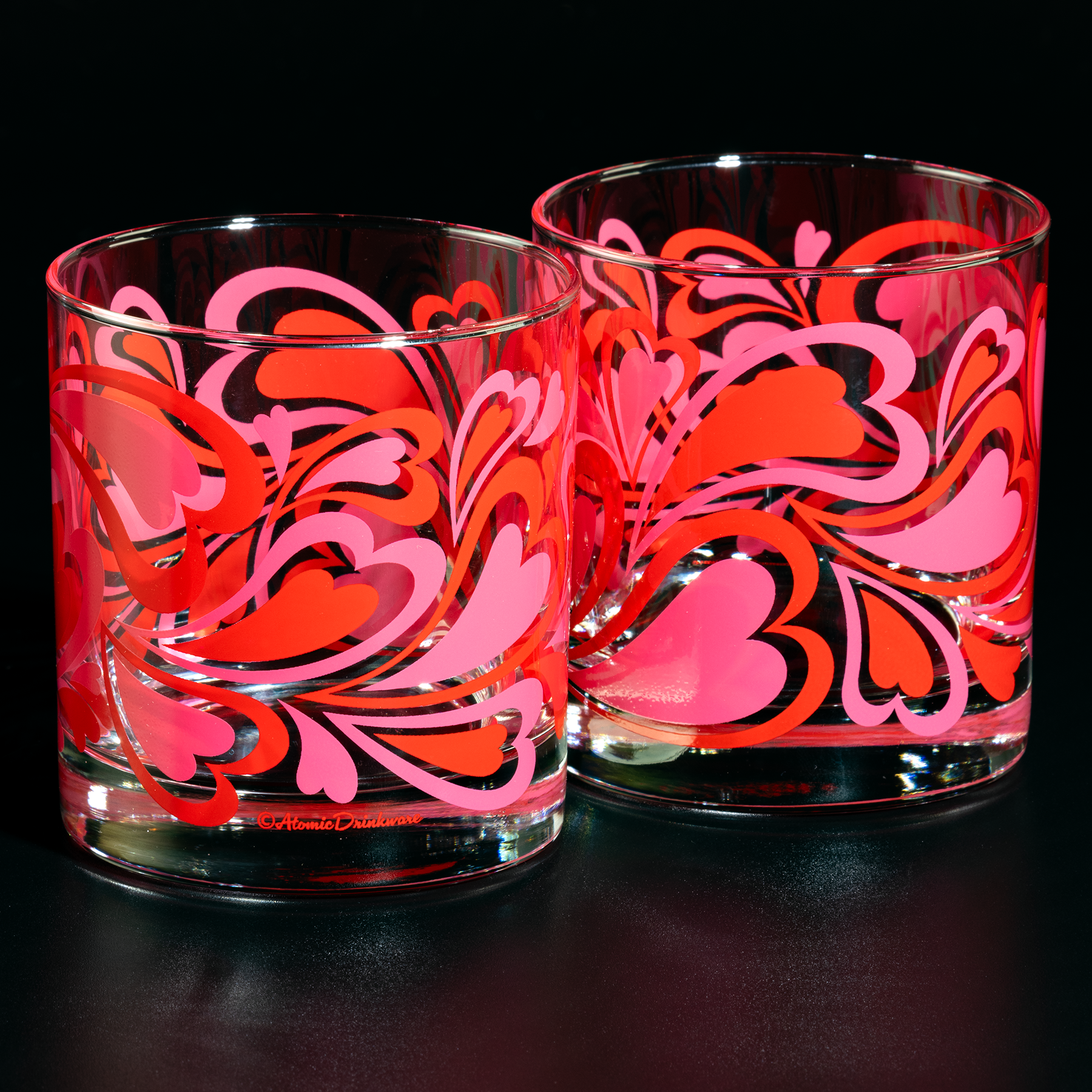 Two glass tumblers with pink and red heart patterns on a black background