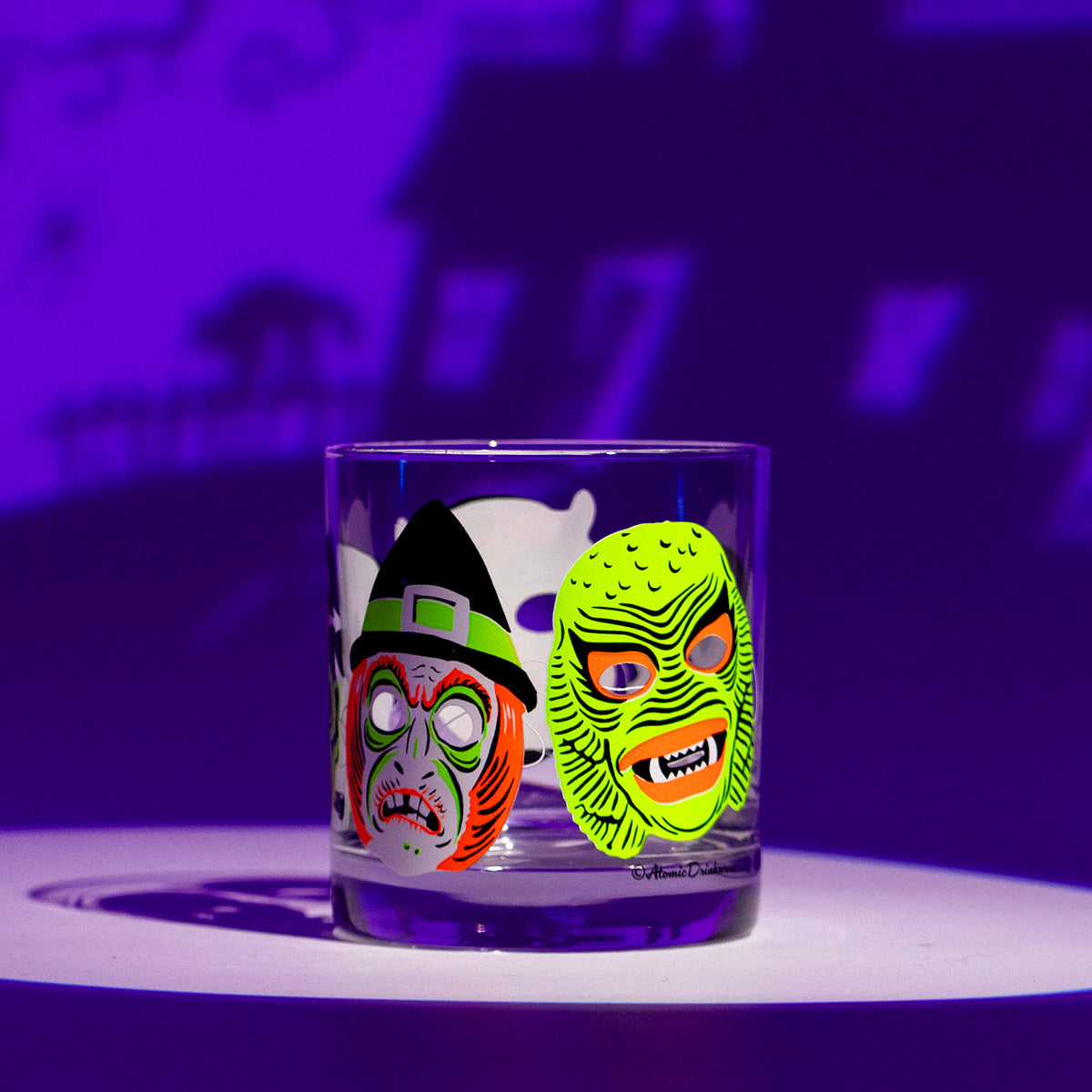 A single Neon Nightmares Rocks glass on a shadowy purple background. Design features screen-printed retro Halloween monster masks