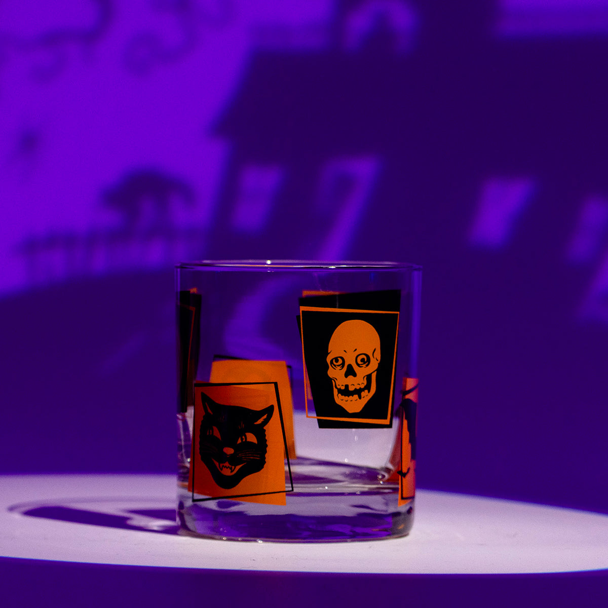 Monster Mash Rocks glass with retro orange and black Halloween screen-printed designs, owl, bats, black cat, skull, jack-o-lantern, and vampire on a Halloween themed purple background.