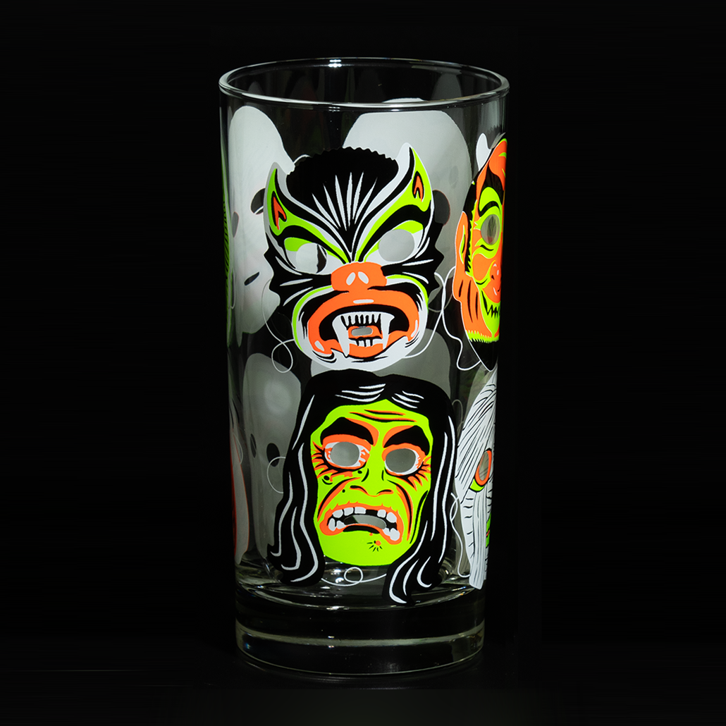 Clear Collins glass on black background, showing fluorescent green and orange retro Halloween cat and hag witch mask