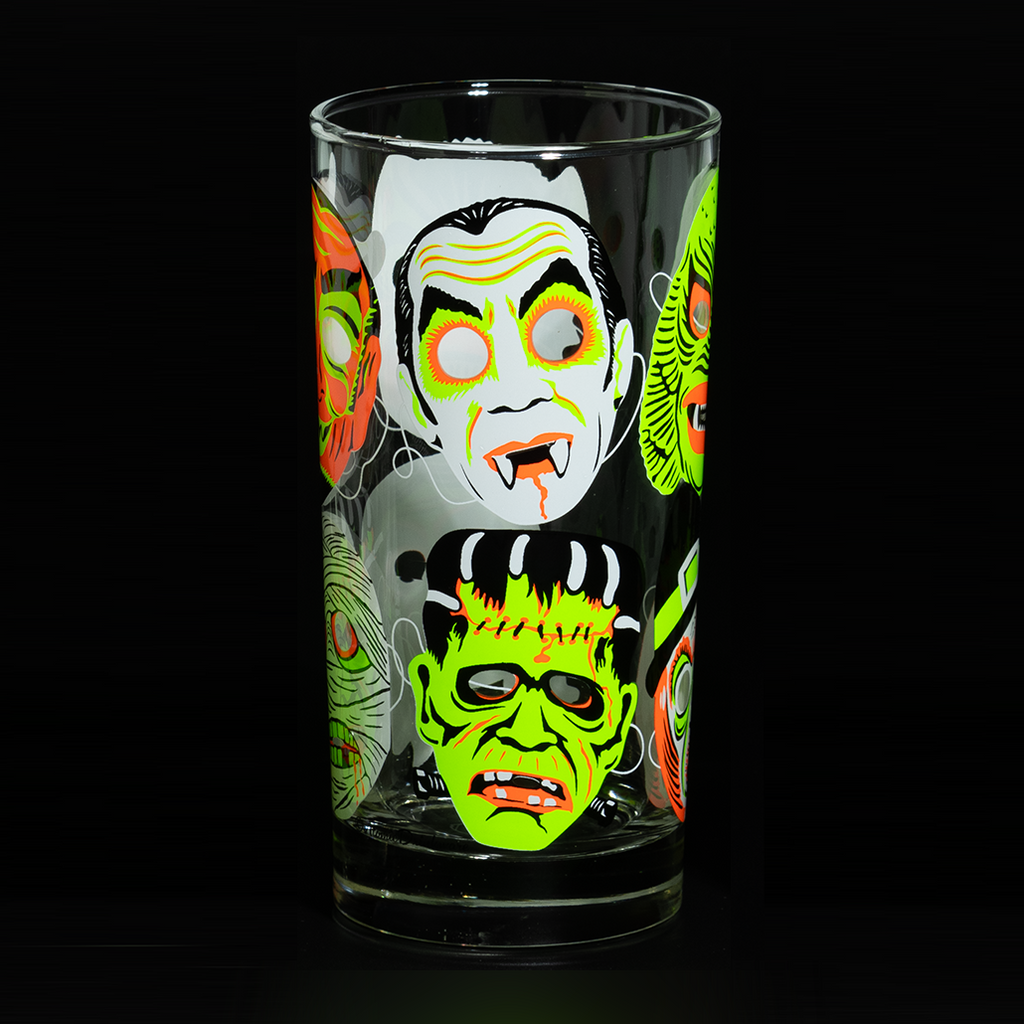Clear Collins glass on black background, showing fluorescent green and orange retro Halloween vampire dracula and frankenstein monster mask