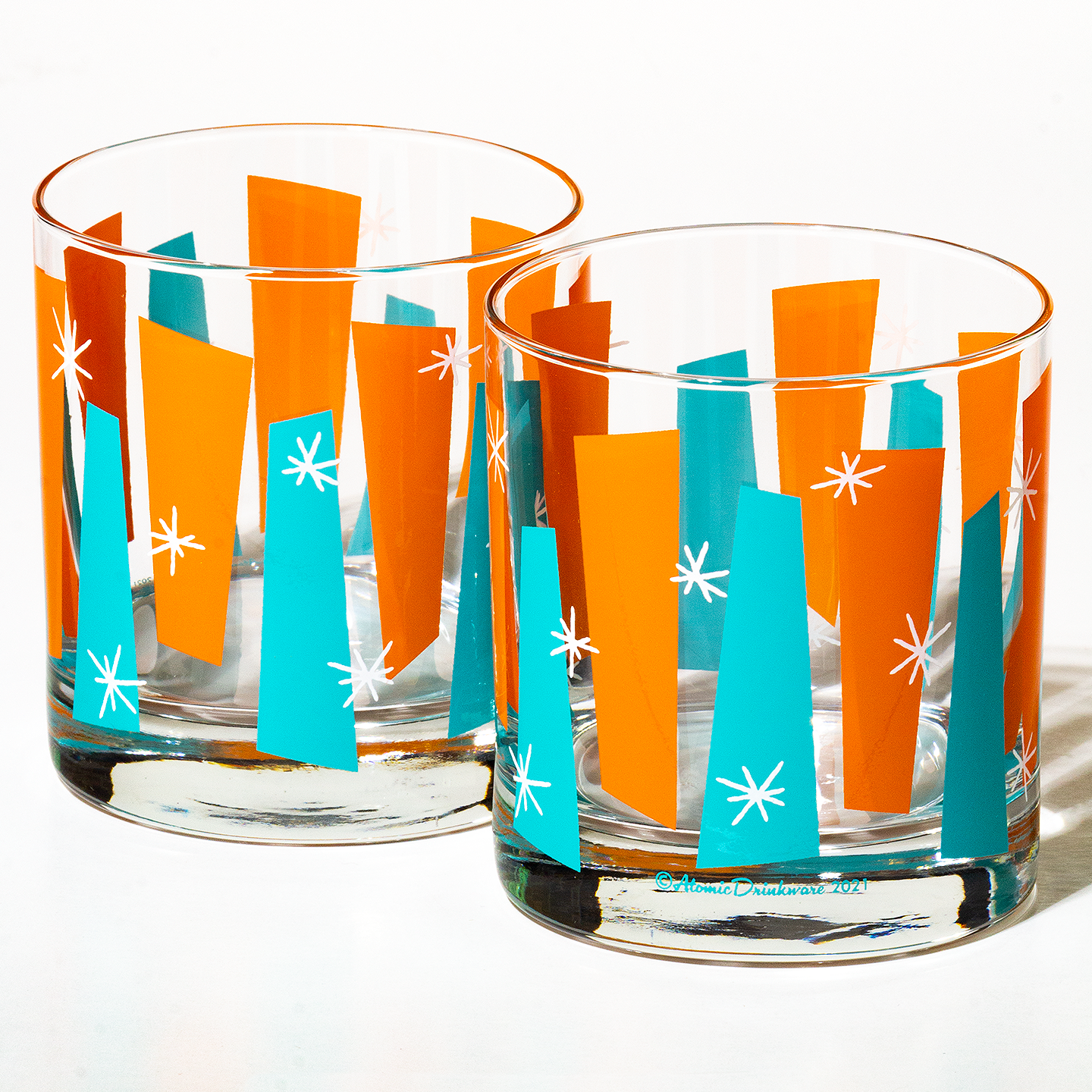 Two glass tumblers with orange and blue geometric pattern and white starbursts on a white background. As seen in House of the Retro Suite, Howard Johnson Anaheim