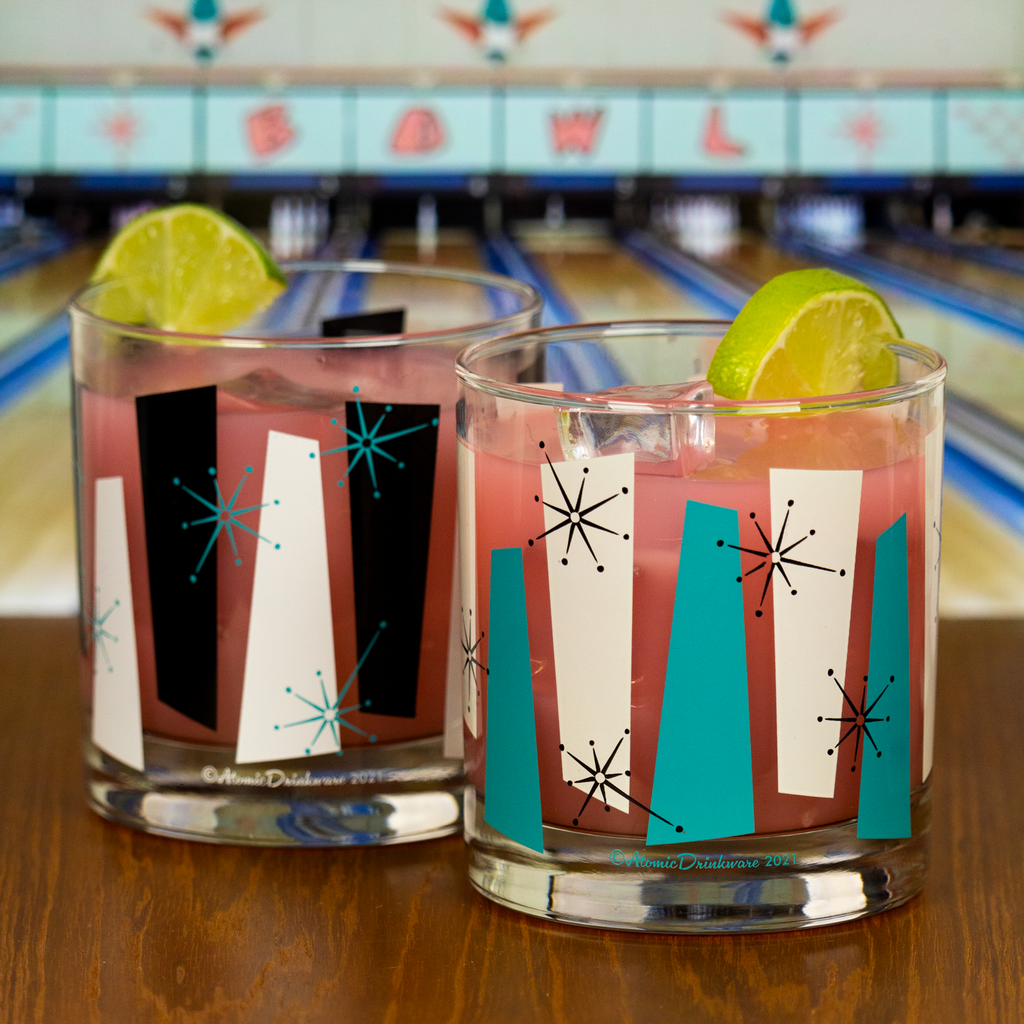 Two retro-style glasses with colorful rock a billy designs on a bowling alley counter.