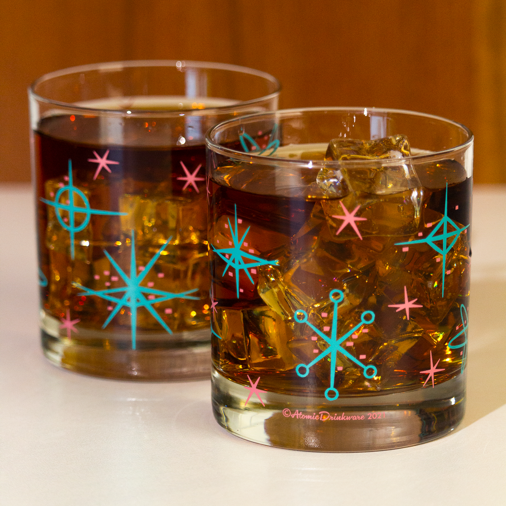 Two retro mid century style glasses of iced drinks with decorative ice cubes on a white surface.