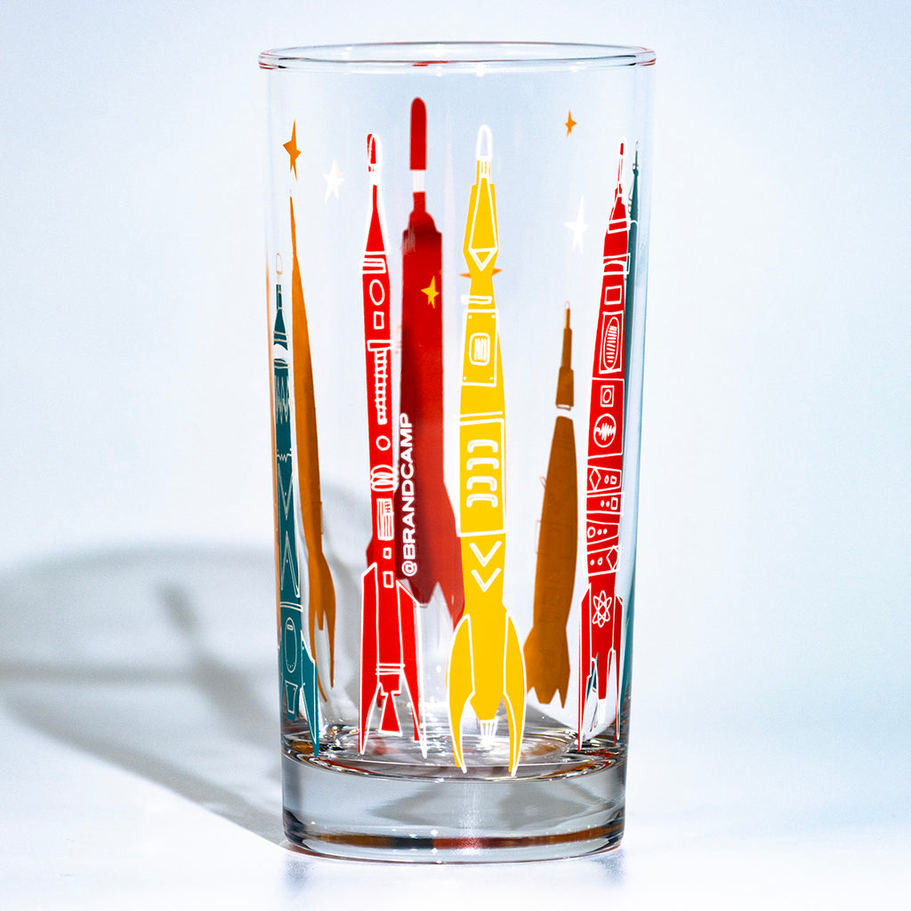 Clear glass tumbler with colorful rocket illustrations on a white background