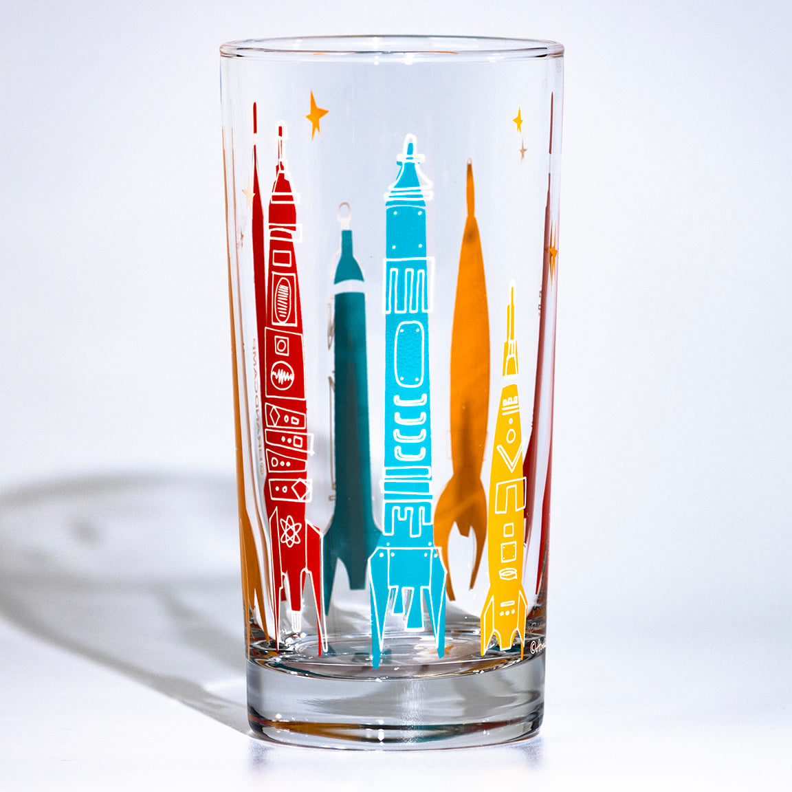 Clear glass tumbler with colorful rocket illustrations on a white background