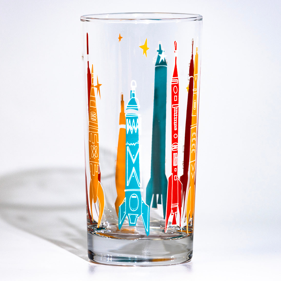 Clear glass tumbler with colorful rocket designs on a white background