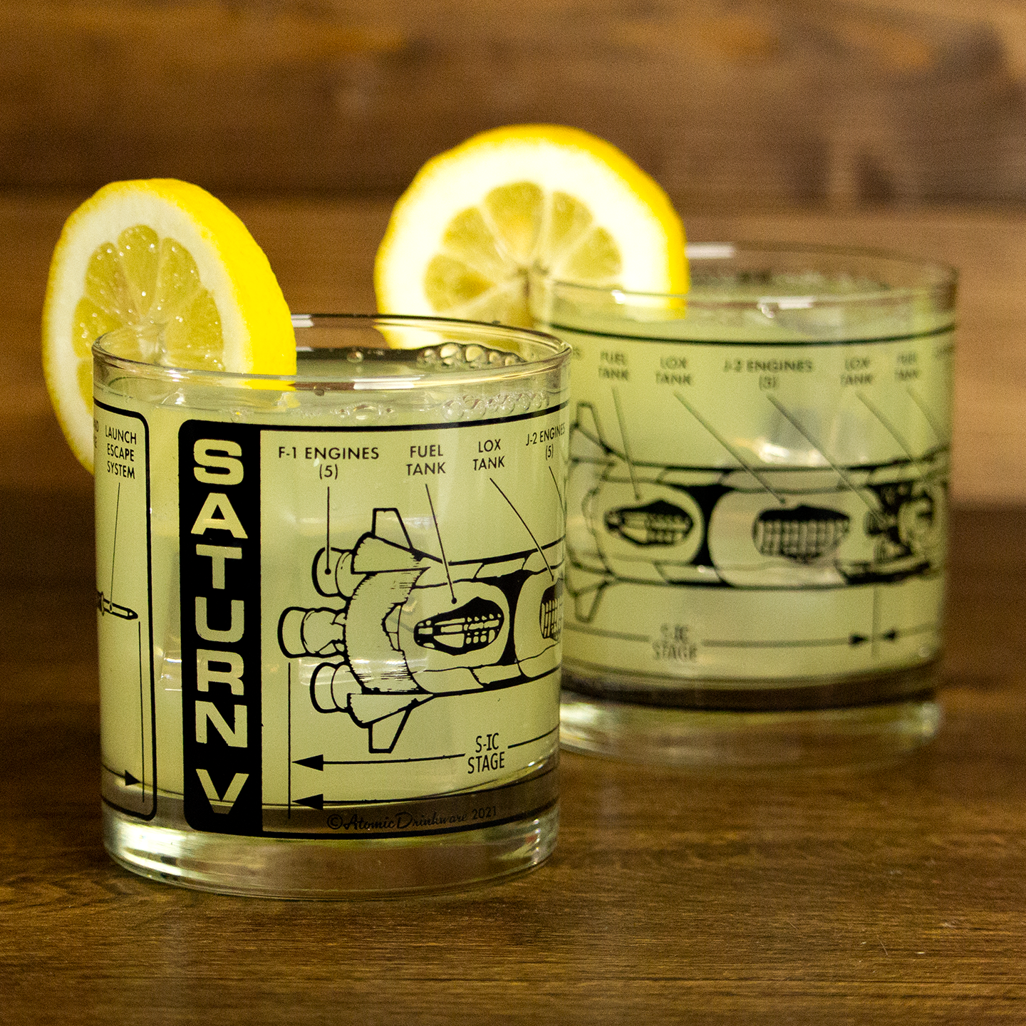 Two glass tumblers with Saturn V rocket design and lemon slices on a wooden surface.