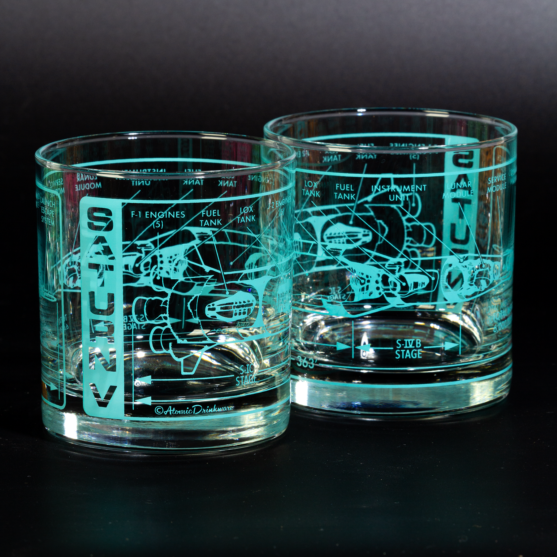 Two glass tumblers with engraved Saturn V rocket design on a black background