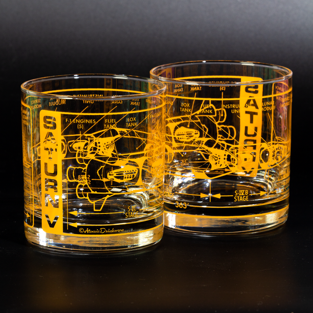 Two clear glasses with yellow Saturn V rocket blueprint engraving on a black background