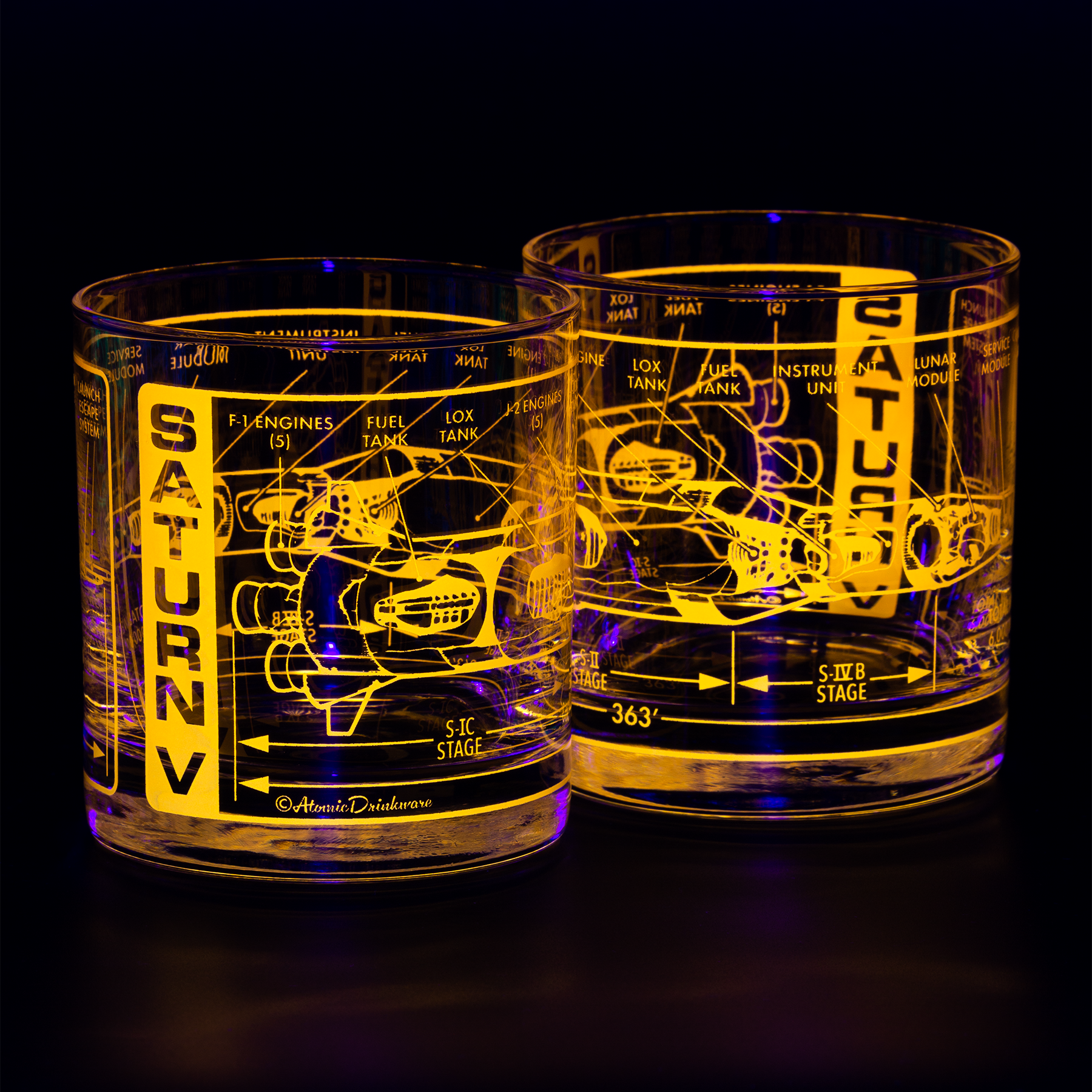 Two glass tumblers with Saturn V rocket blueprint engraving on a black background