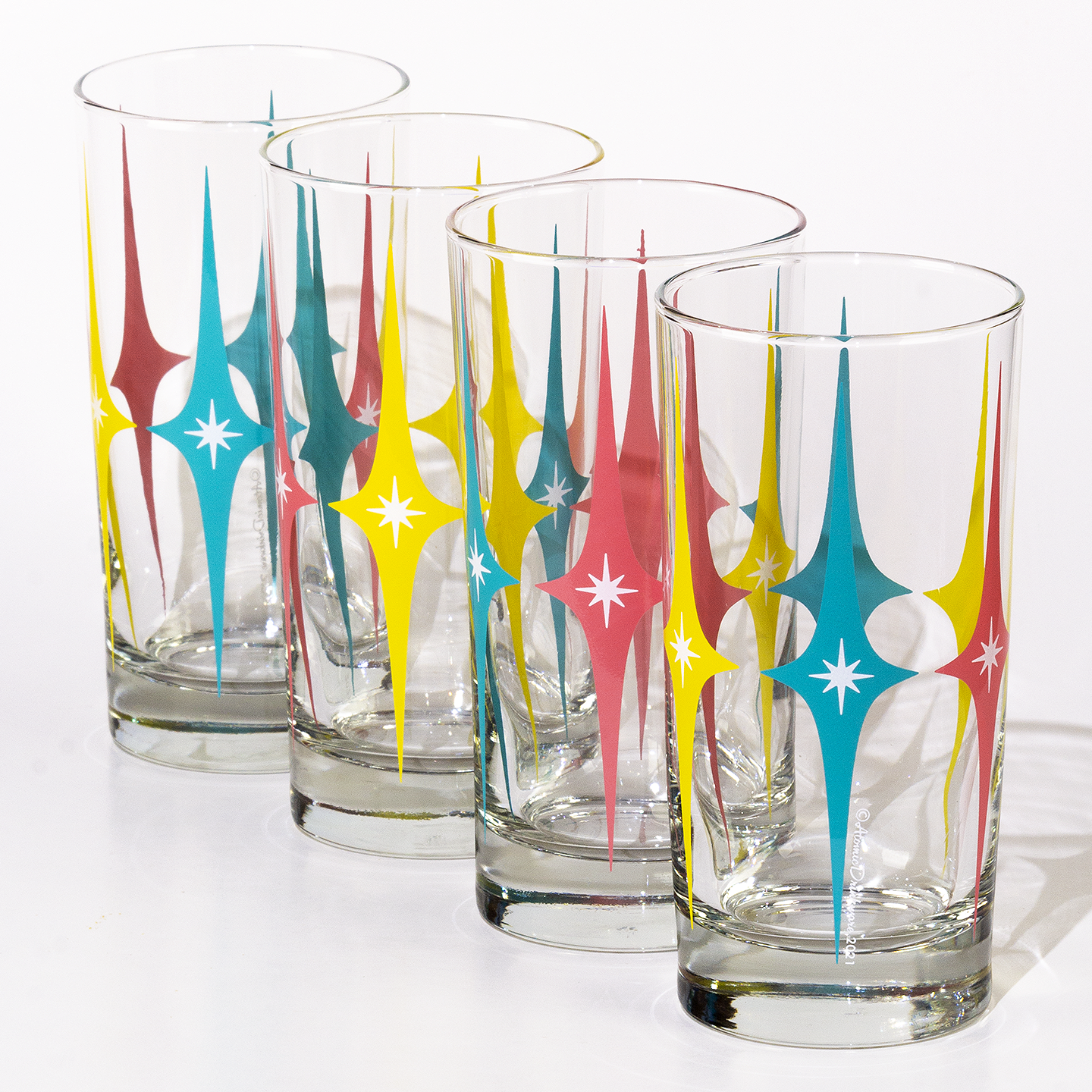Set of four glass tumblers with colorful retro starburst designs for home barware or collectors item