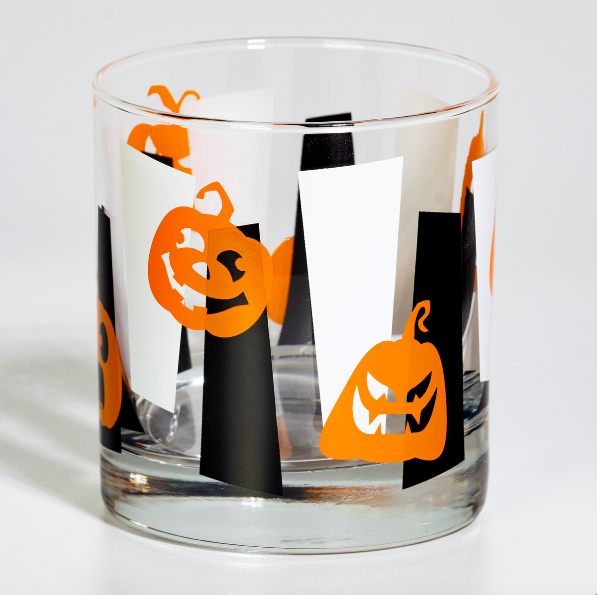 A clear glass tumbler with a Halloween-themed pattern of orange jack-o'-lanterns and black-and-white striped shapes, shown on a white background.