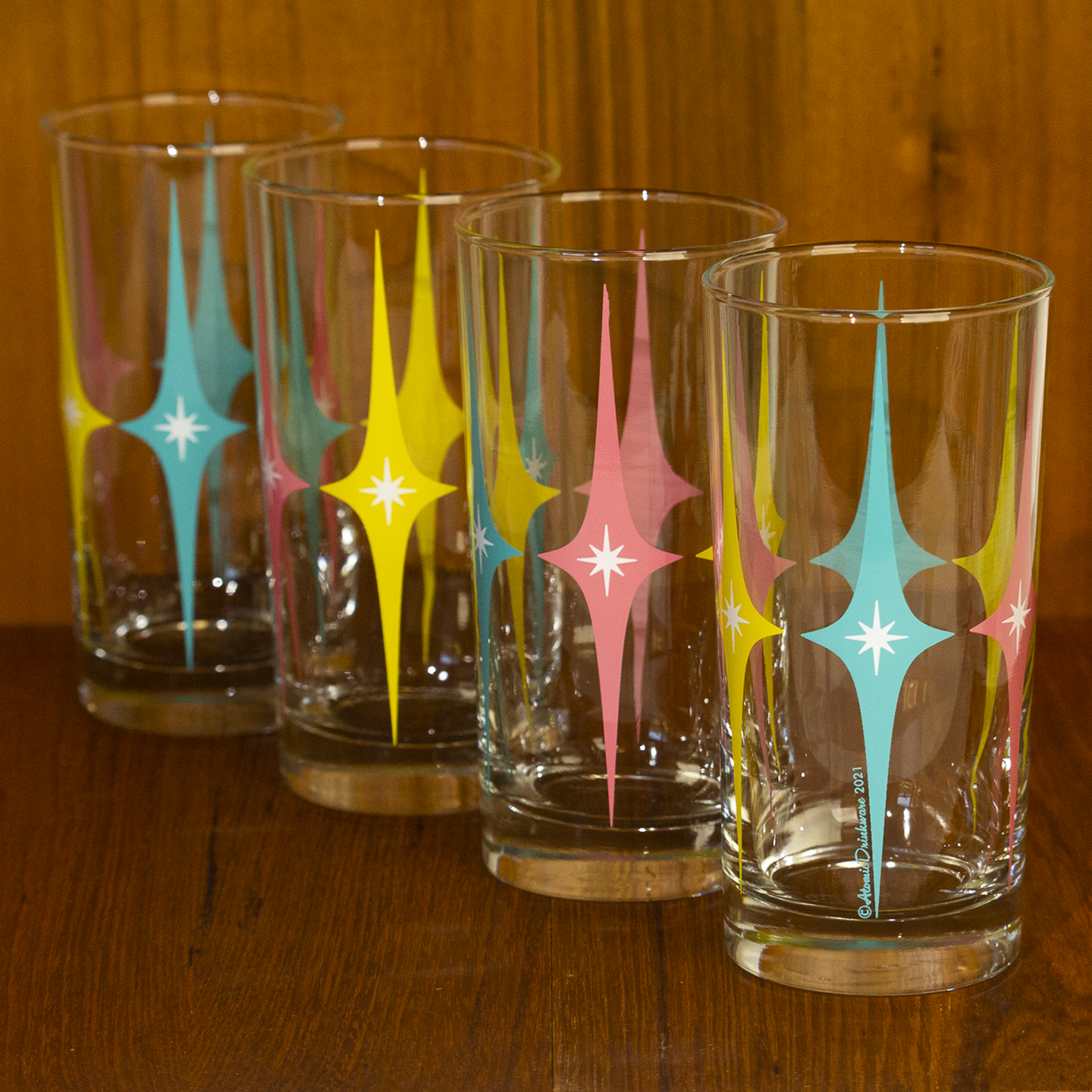 Four glass tumblers with colorful retro geometric designs on a wooden surface