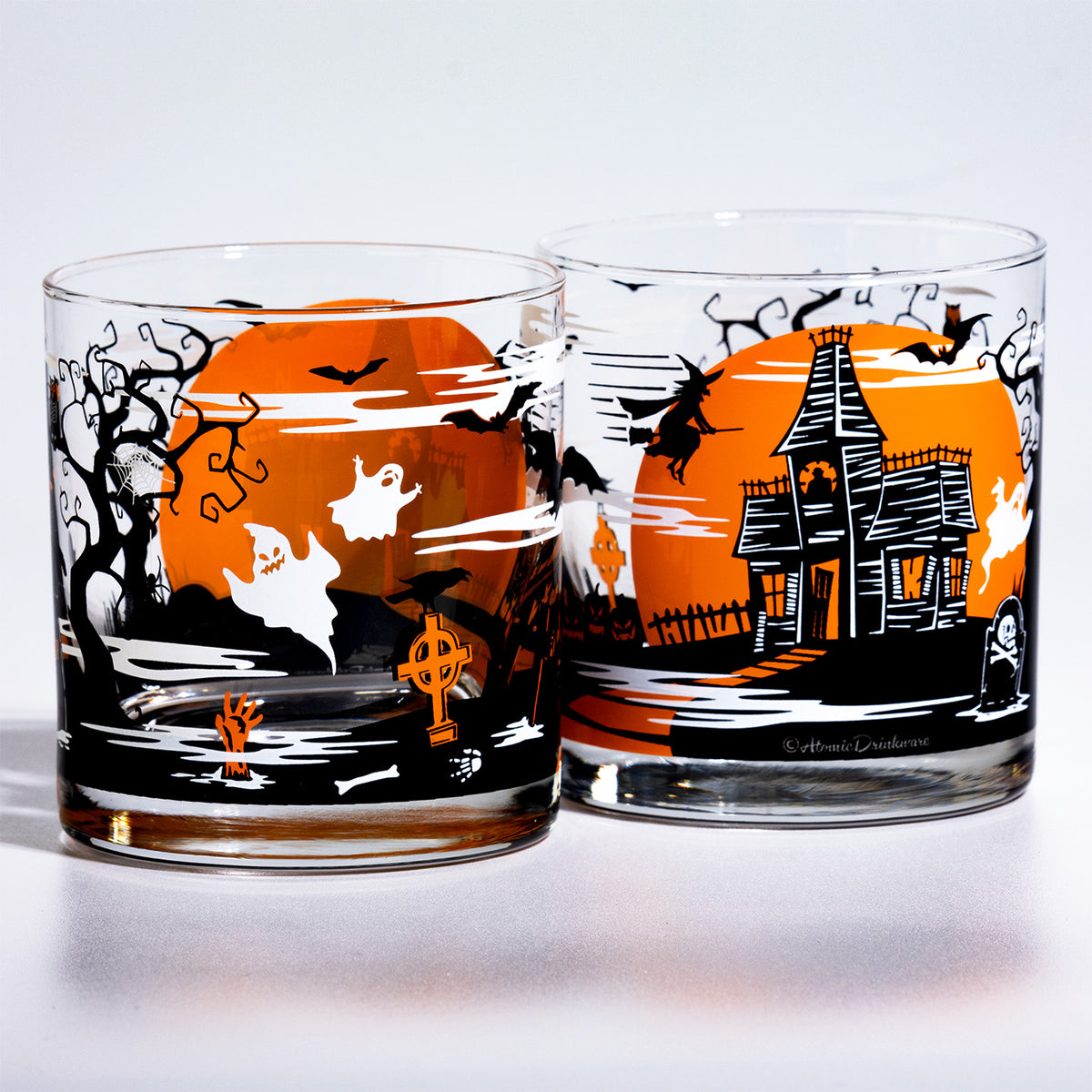 Two clear glass rocks with a Halloween landscape print featuring an orange full moon, black bats, a haunted house, ghosts, and bare trees, shown on a white background.