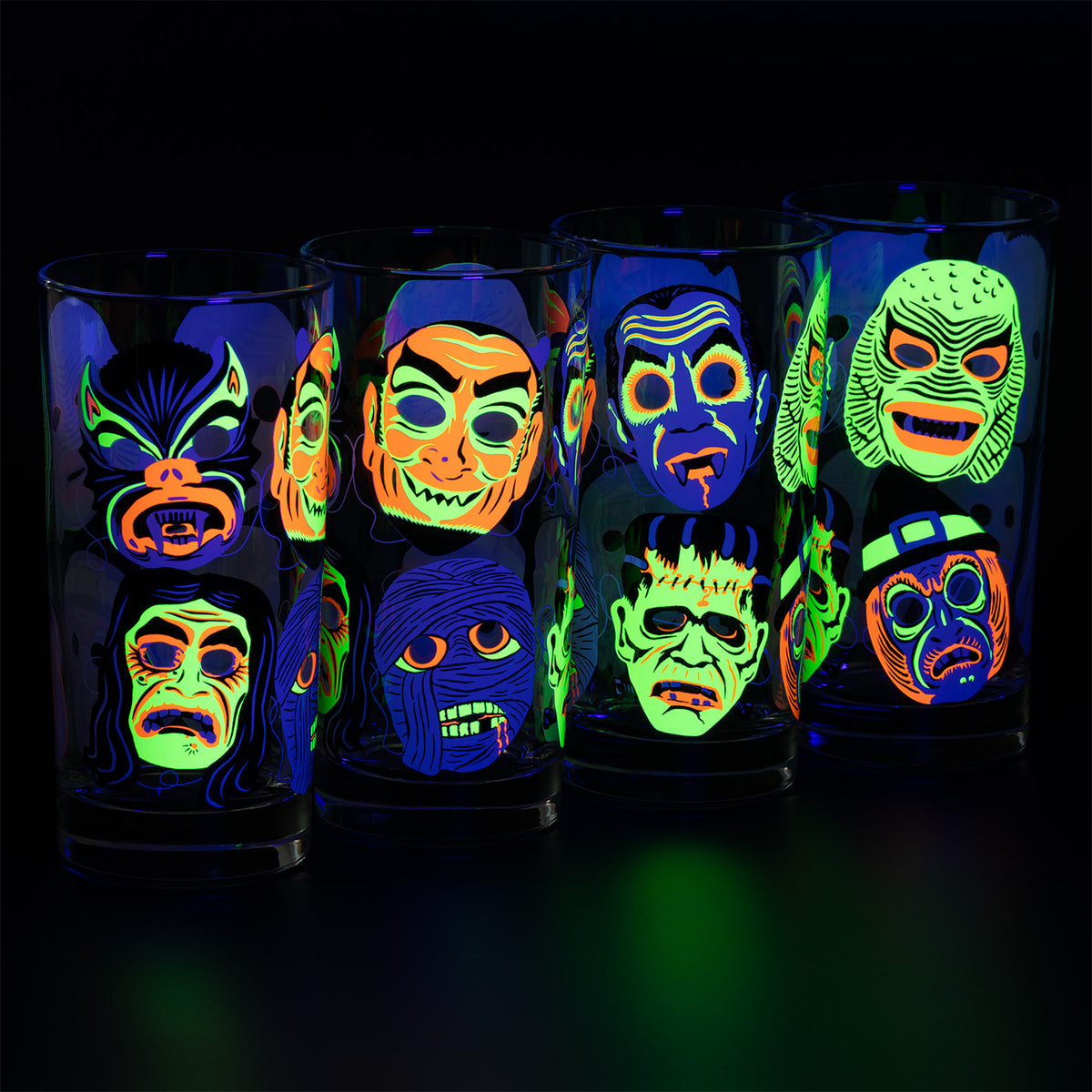 Four lined up Neon Nightmare Collins glasses with screen printed retro monster masks glowing fluorescent under a blacklight on a black background. 