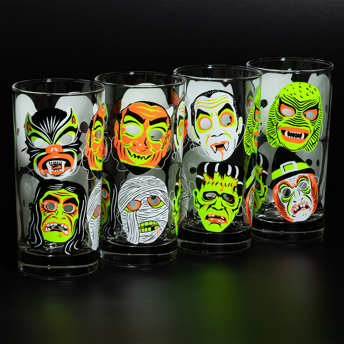 Four lined up Neon Nightmare Collins glasses with screen printed retro monster masks on a black background. 