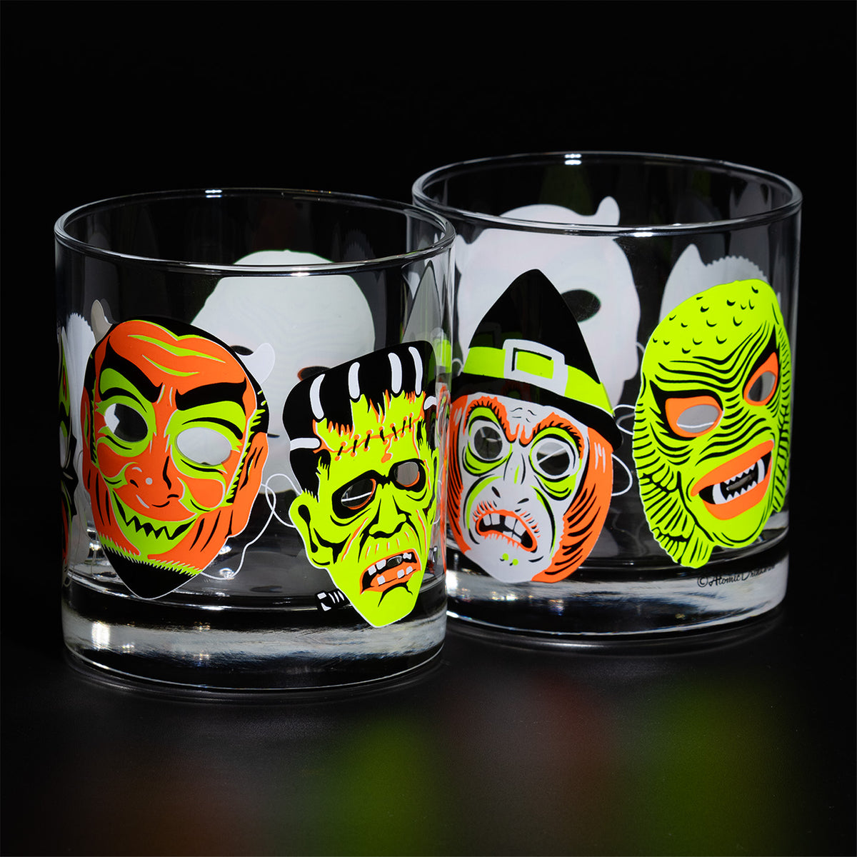 Two lined up Neon Nightmares Rocks glasses with screen printed retro monster masks on a black background. 