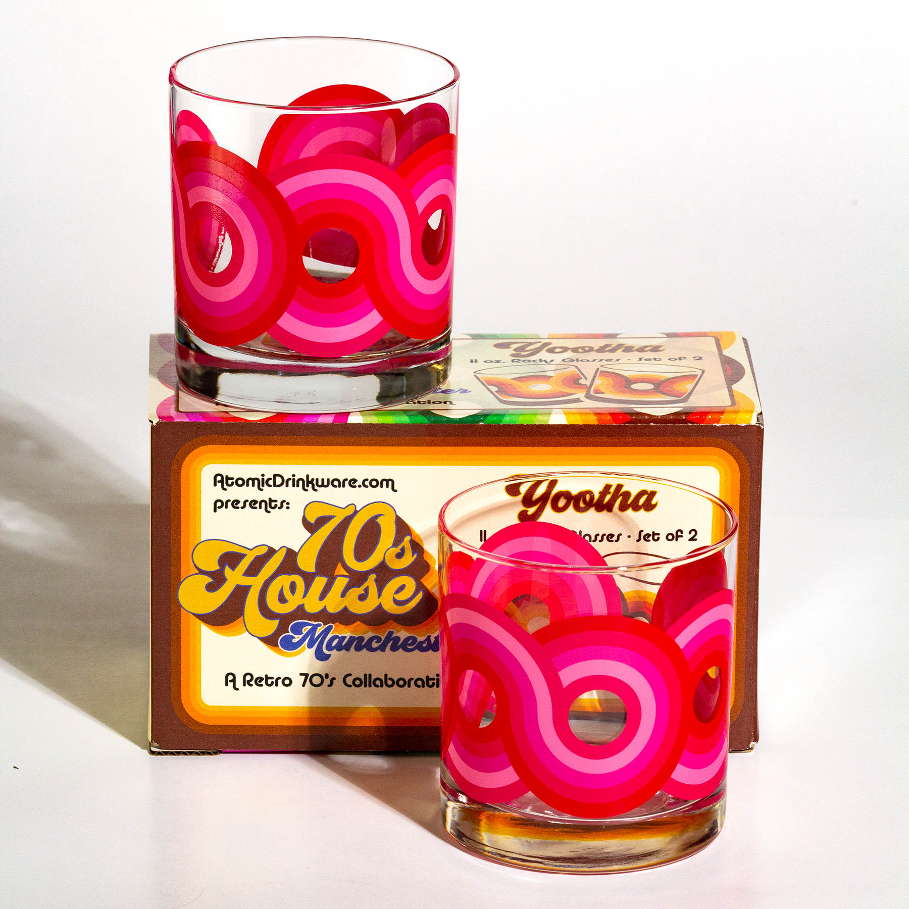 Two retro-style glasses with pink and red designs on a box labeled '70s House Manchester' by AtomicDrinkware.com.