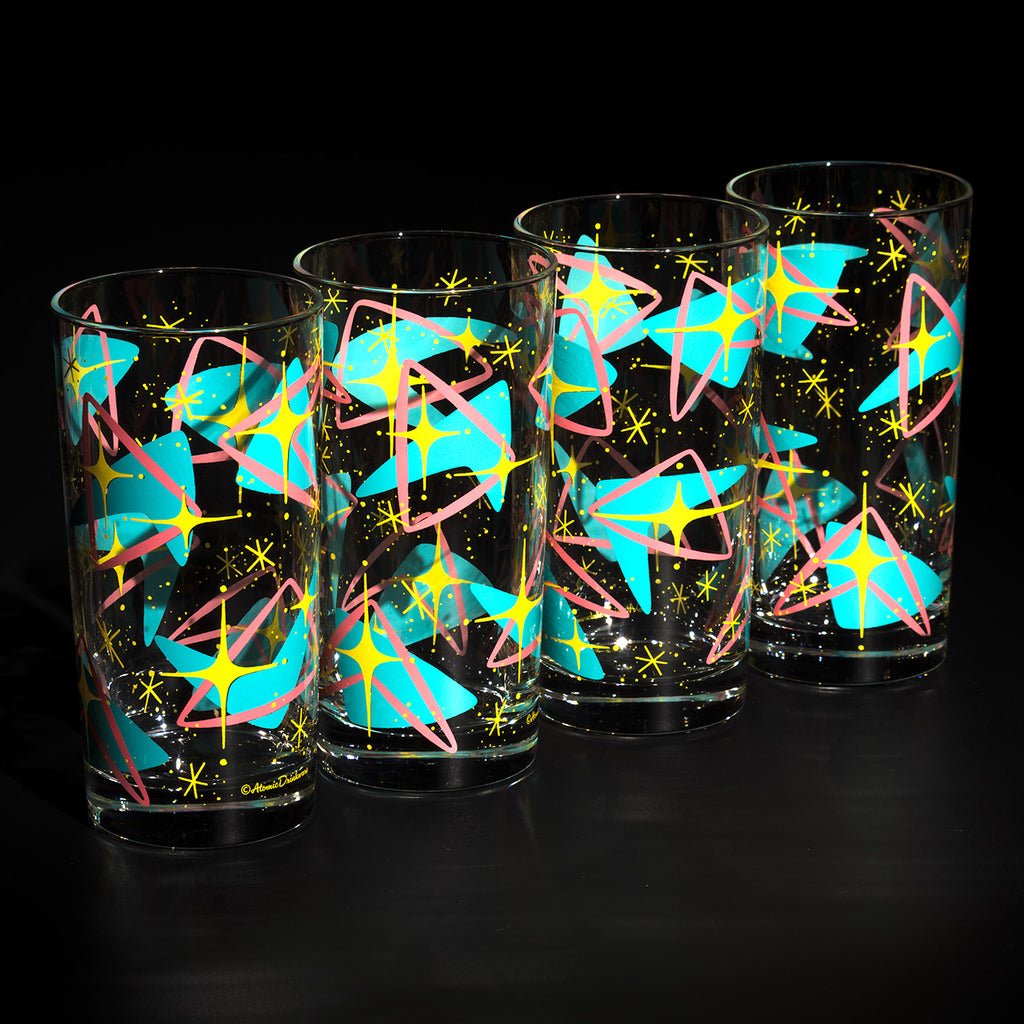 Four clear drinking glasses with a 1960s or 1970s retro pattern of glowing cyan, pink, and yellow starbursts on a black background. Atomic style retro barware