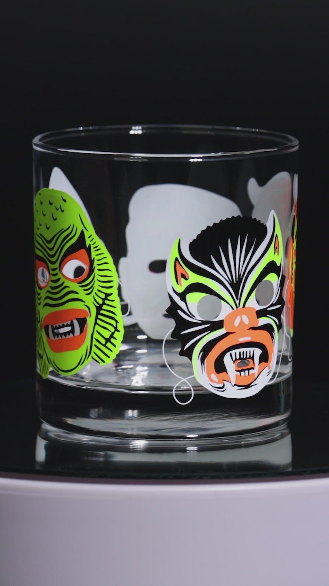 Two glass tumblers with colorful  retro halloween mask designs on a black background